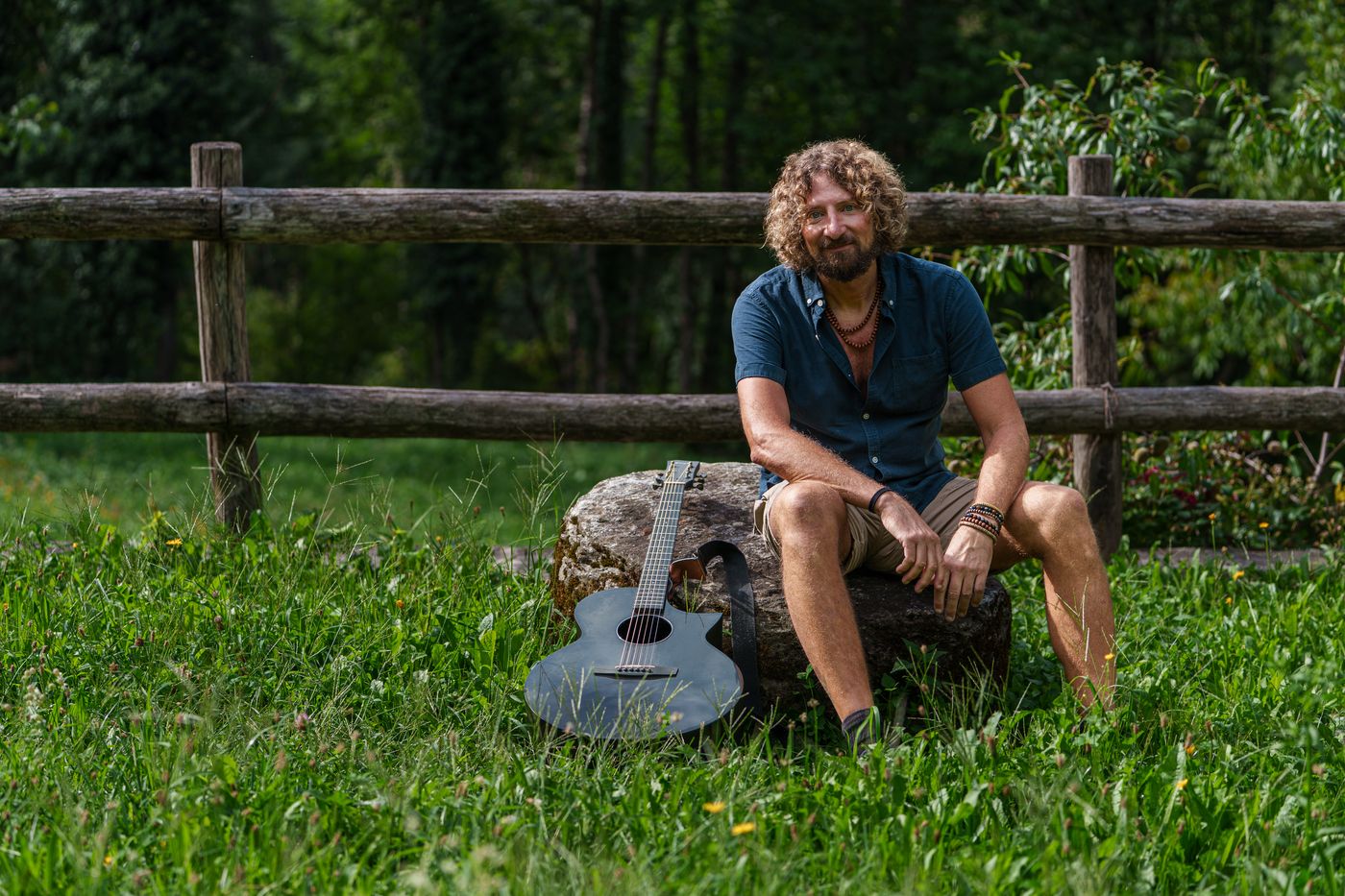 Pat sitting on a fence rail with guitar